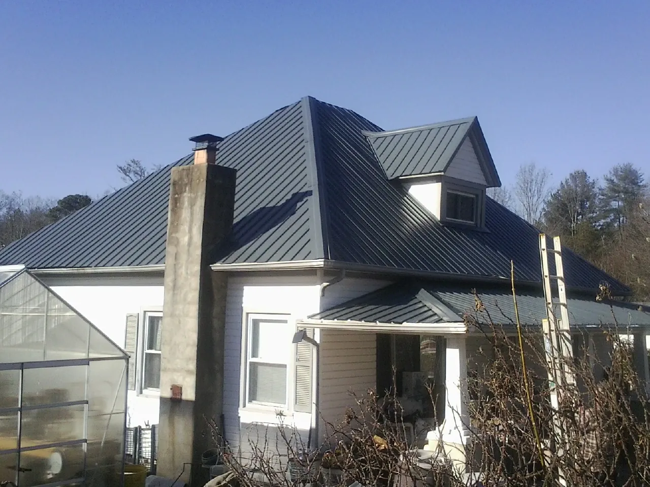Dark blue standing seam metal roof on a white farmhouse with dormer — Slate & Tile Roof Repair by Roofing Brothers in Felt