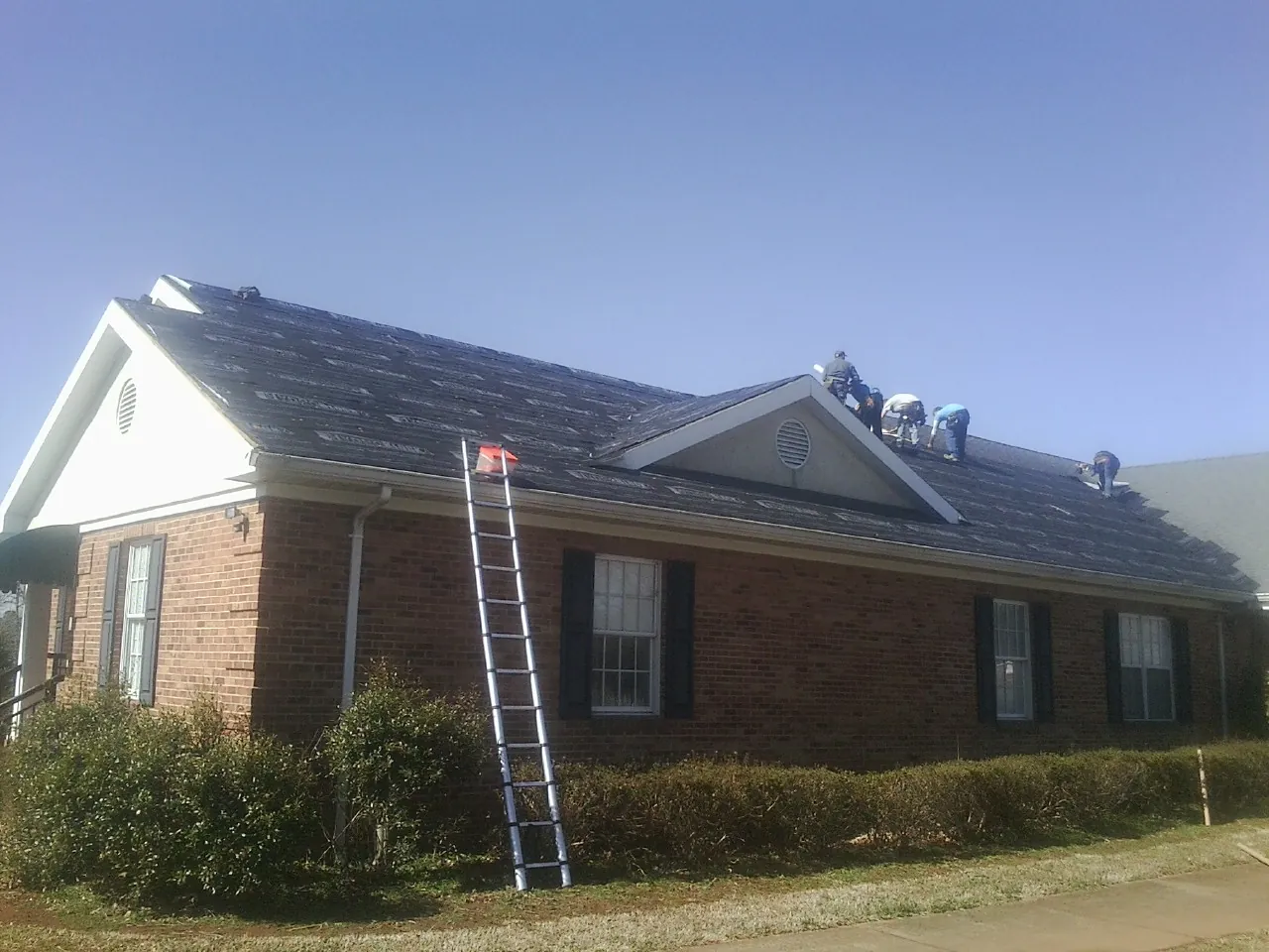 Crew tearing shingles off a brick ranch roof with a ladder set — Emergency Roof Repair work by our crew in Felt