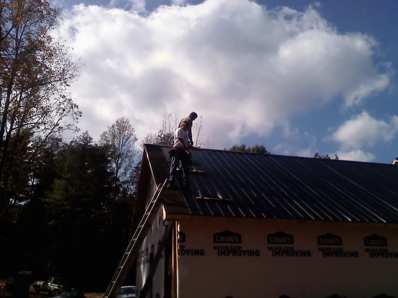 Roofer fastening dark metal panels high against a cloudy sky, from a Roof Inspection job in Felt